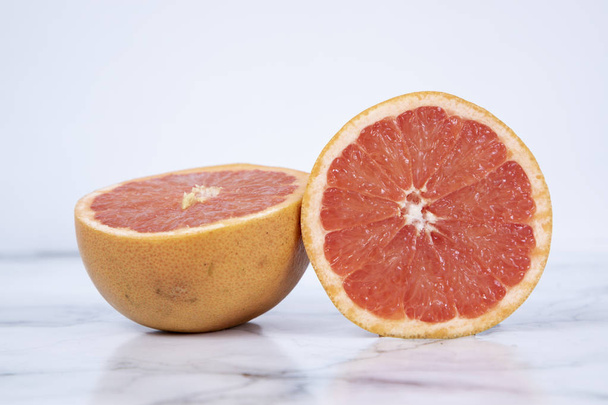 Split grapefruit on a marble table and white background - Zdjęcie, obraz