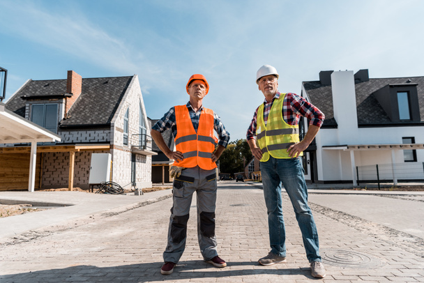 строители среднего возраста, стоящие с руками на бедрах снаружи
  - Фото, изображение
