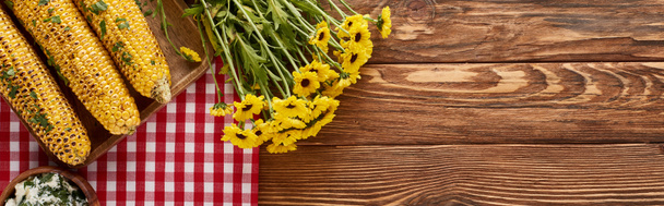 Şükran Günü yemeği için ahşap masada sarı çiçeklerin yanında servis edilen ızgara mısırın üst görüntüsü, panoramik çekim. - Fotoğraf, Görsel