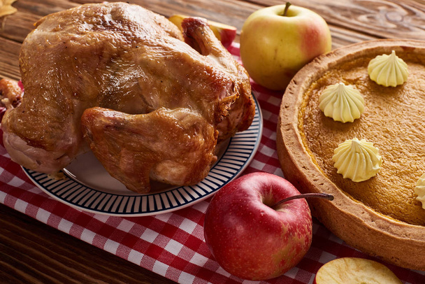 カボチャのパイ,ロースト七面鳥とリンゴの赤チェッカードナプキンの木のテーブルで感謝祭のディナー - 写真・画像
