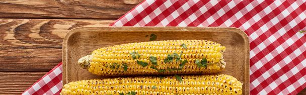 top view of grilled corn served on red checkered napkin at wooden table for Thanksgiving dinner, panoramic shot - Fotó, kép