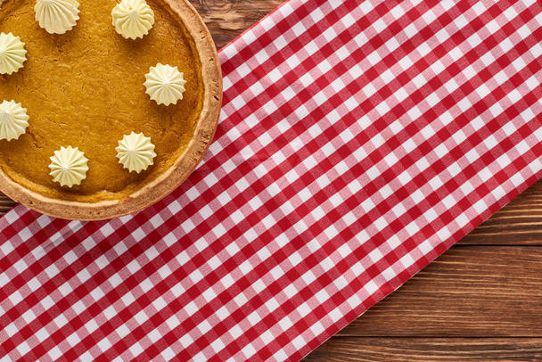 top view of traditional pumpkin pie on red checkered napkin at wooden table for Thanksgiving dinner - Fotó, kép