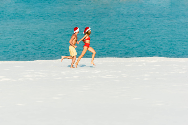 sexy girlfriend and boyfriend in santa hats running on beach in Maldives  - Фото, изображение