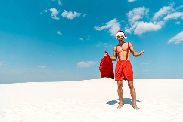 шокований і сексуальний чоловік у капелюсі в Санті, який тримає мішок на пляжі на Мальдівах  - Фото, зображення
