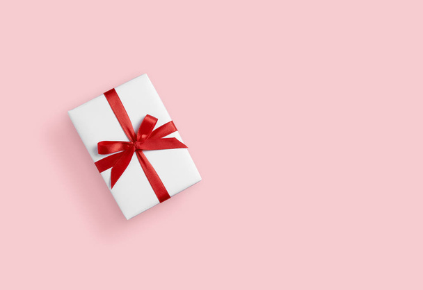 Top view of white gift box with red ribbon on pink isolated back - Foto, Imagen