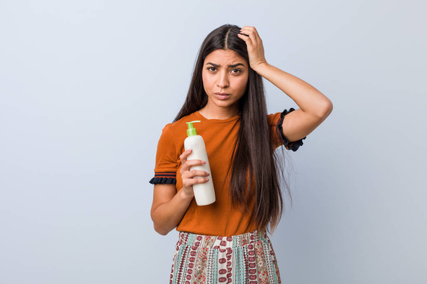 Young arab woman holding a cream bottle being shocked, she has remembered important meeting. - Foto, Bild