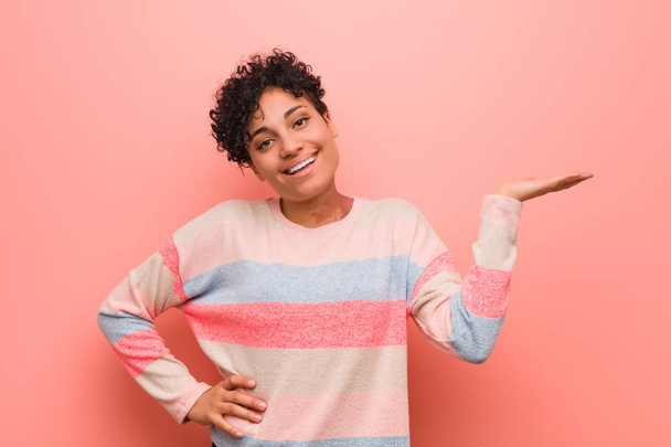 Jeune femme adolescente afro-américaine mixte montrant un espace de copie sur une paume et tenant une autre main à la taille
. - Photo, image