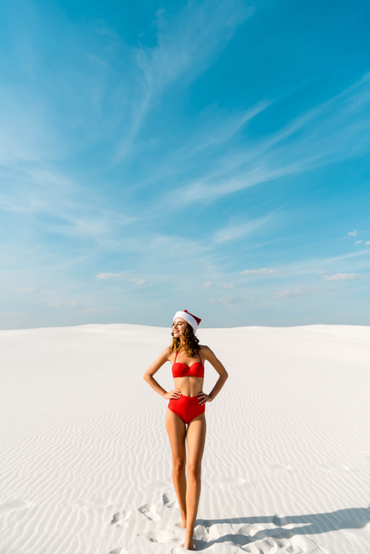 sexy and smiling woman in santa hat and swimsuit with hands on hips on beach in Maldives  - Φωτογραφία, εικόνα