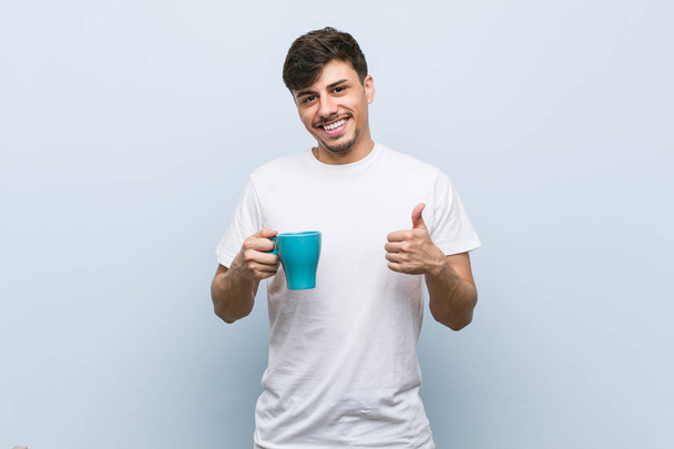 Young hispanic man holding a cup smiling and raising thumb up - Фото, изображение