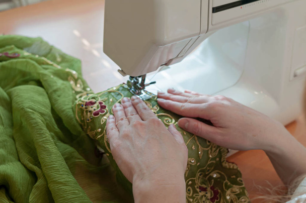 cropped view of seamstress tailoring green cloth with sawing machine at table in studio - Фото, изображение