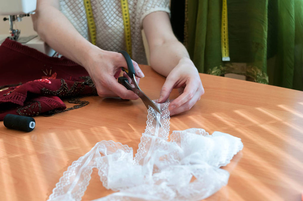 crpped view of woman cutting white lace with scissors on wooden table near red cloth in studio  - Foto, imagen