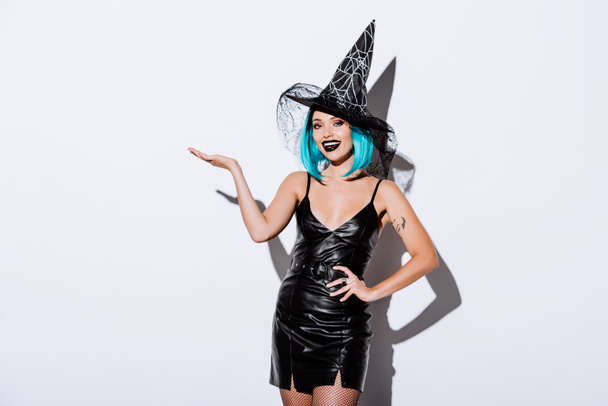 happy girl in black witch Halloween costume with blue hair pointing with hand on white background - Fotoğraf, Görsel