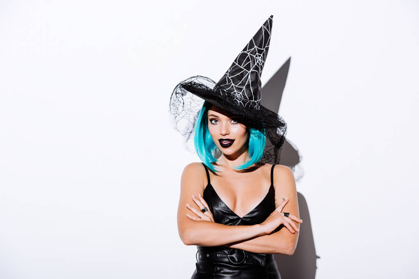 Siyah Cadı Cadılar Bayramı kostümlü, mavi saçlı, kollarını çapraz beyaz arka planda tutan bir kız. - Fotoğraf, Görsel