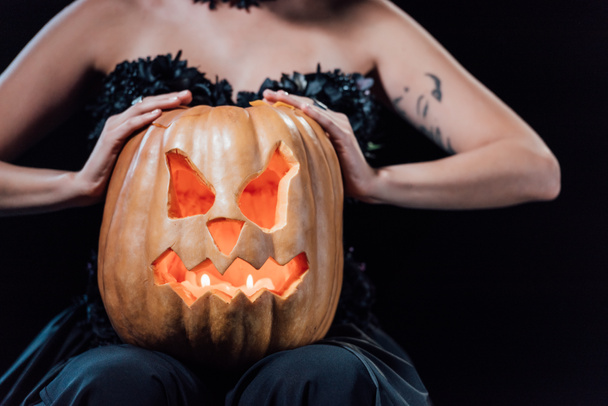 cropped view of girl in black gothic dress holding carved Halloween pumpkin with candles isolated on black - Valokuva, kuva