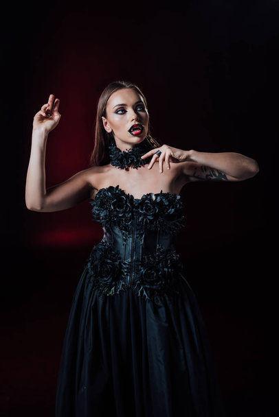 straszny wampir dziewczyna z kłami w czarny gotycki strój na czarnym tle - Zdjęcie, obraz