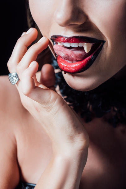 cropped view of scary vampire girl licking fangs isolated on black - Foto, afbeelding