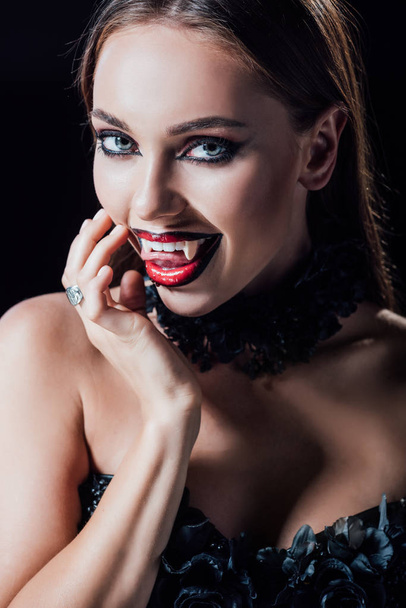 scary vampire girl showing fangs in black gothic dress isolated on black - Photo, Image