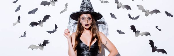 panoráma lövés a lány fekete boszorkány Halloween jelmez közelében fehér fal dekoratív denevérek - Fotó, kép