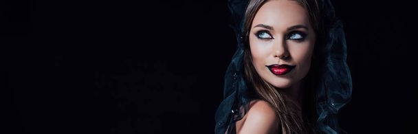 panoramic shot of scary vampire girl in black gothic dress and veil looking away isolated on black - 写真・画像