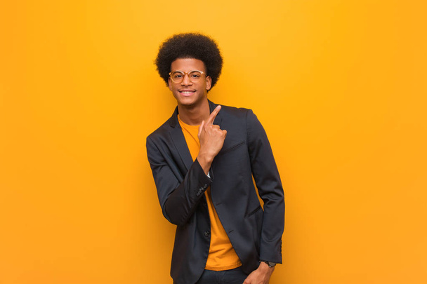 junger unternehmer afrikanisch-amerikanischer mann über eine orangefarbene wand lächelnd und zur seite zeigend - Foto, Bild