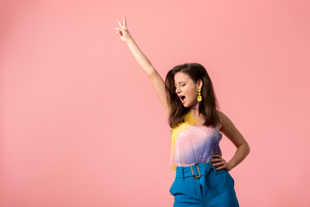 aufgeregtes junges stilvolles Disco-Mädchen tanzt mit der Hand in der Luft isoliert auf rosa - Foto, Bild
