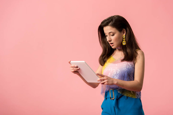 shocked young stylish disco girl holding digital tablet isolated on pink - Photo, Image