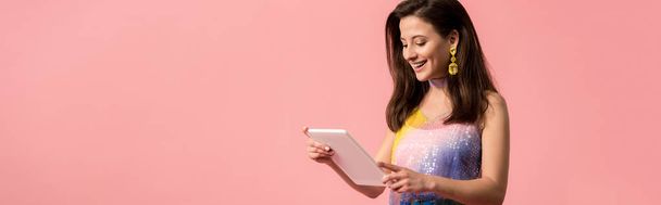 panoramic shot of happy young stylish disco girl holding digital tablet isolated on pink - Foto, Imagem