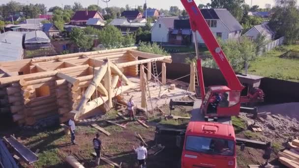 Crane lifts on cables wooden structure. Clip. Top view of process of building wooden country house with crane. Crane lifts design of facade of wooden roof - Footage, Video