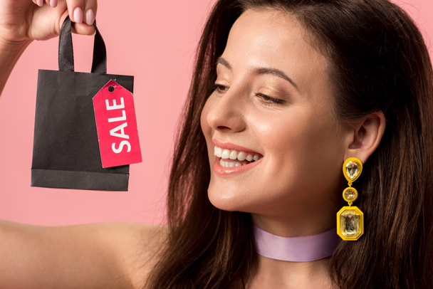 щаслива стильна дівчина дискотека тримає сумку з продажем на етикетці ізольована на рожевому
 - Фото, зображення