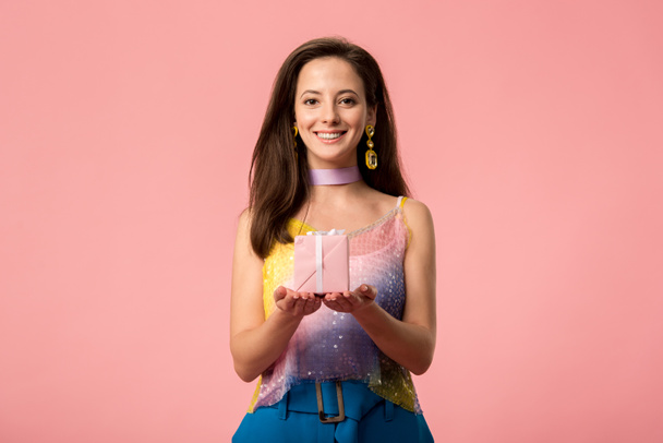 happy young stylish disco girl holding gift box isolated on pink - Foto, afbeelding