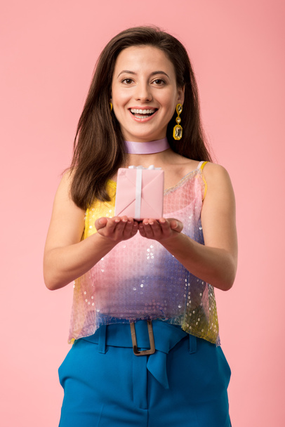happy young stylish disco girl holding gift box isolated on pink - Fotoğraf, Görsel