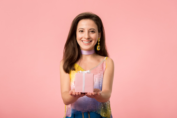 happy young stylish disco girl holding gift box isolated on pink - Фото, изображение