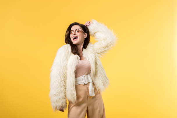 excitada chica de fiesta en chaqueta de piel sintética y gafas de sol bailando aislado en amarillo
 - Foto, Imagen