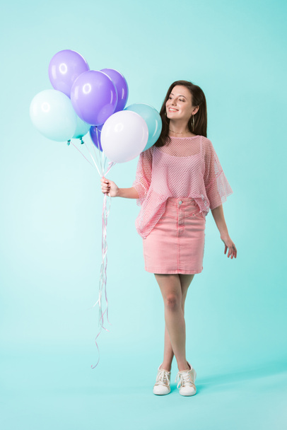 smiling girl in pink outfit holding balloons on turquoise background - Foto, afbeelding