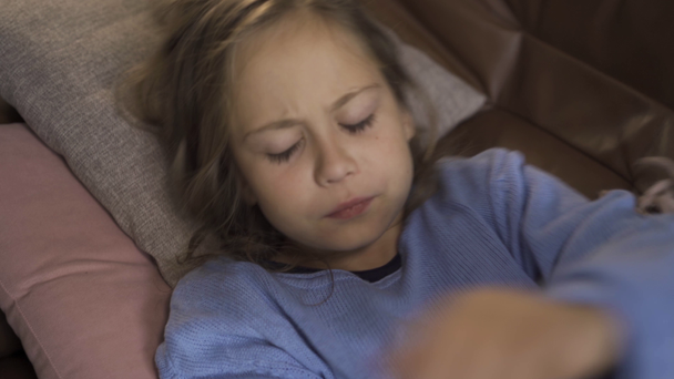 Close-up face of sick caucasian girl sneezing while lying under blanket at home. The sad child has fever. Concept of health, illness, sickness, common cold, treatment - Materiał filmowy, wideo