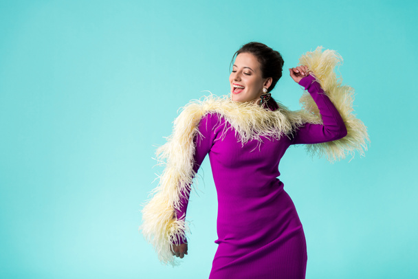 podekscytowany strona dziewczyna w fioletowy sukienka z piór taniec odizolowany na turkusowy  - Zdjęcie, obraz