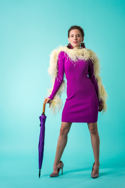 party girl in purple dress with feathers holding umbrella on turquoise  - Photo, Image