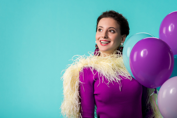 happy party meisje in paars jurk met veren houden ballonnen geïsoleerd op turquoise  - Foto, afbeelding