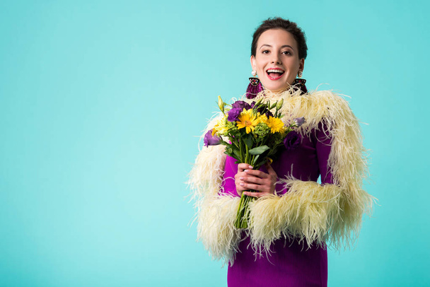 happy party girl in purple dress with feathers holding bouquet of flowers isolated on turquoise  - 写真・画像