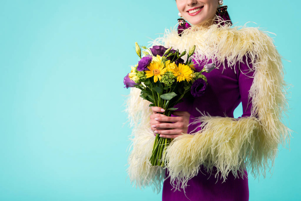 cropped view of smiling party girl in purple dress with feathers holding bouquet of flowers isolated on turquoise  - Photo, Image
