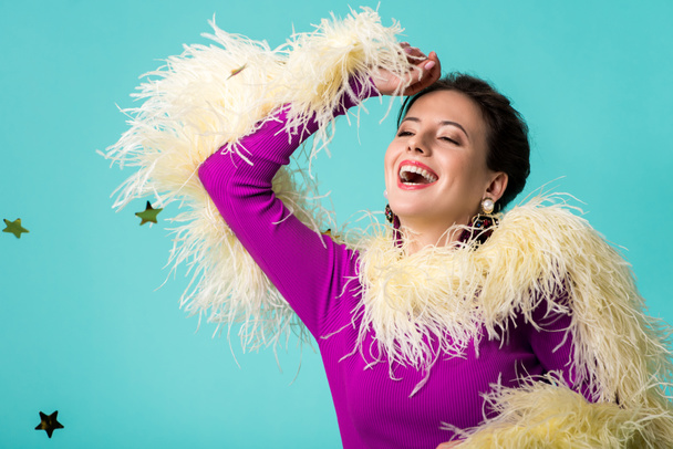 happy party girl in purple dress with feathers under falling confetti isolated on turquoise  - 写真・画像