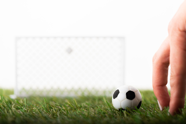 обрезанный вид женских пальцев рядом с игрушечными футбольными воротами и мячом на зеленом поле, изолированный на белом, концепция ставок на спорт
 - Фото, изображение