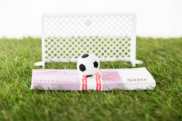 игрушечный футбольный мяч на банкнотах евро возле миниатюрных футбольных ворот на зеленой траве, изолированной на белой, концепция ставок на спорт
 - Фото, изображение