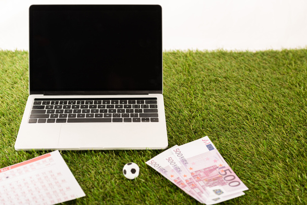 pelota de fútbol de juguete, billetes en euros, listas de apuestas cerca de la computadora portátil con pantalla en blanco sobre hierba verde aislado en blanco, concepto de apuestas deportivas
 - Foto, Imagen
