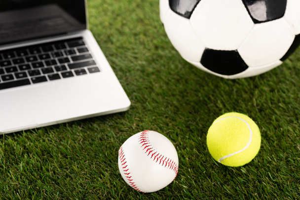 fútbol, béisbol y pelotas de tenis cerca de la computadora portátil en hierba verde, concepto de apuestas deportivas
 - Foto, Imagen