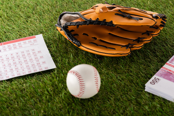 rękawica baseballowa i piłka w pobliżu banknotów euro oraz lista zakładów na zieloną trawę odizolowaną od białej, sportowej koncepcji zakładów - Zdjęcie, obraz