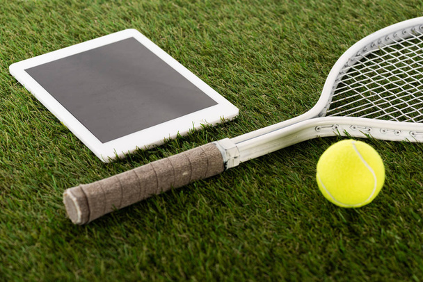 tenisová raketa a míček u digitálního tabletu s prázdnou obrazovkou na zelené trávě, koncept sportovního sázení - Fotografie, Obrázek
