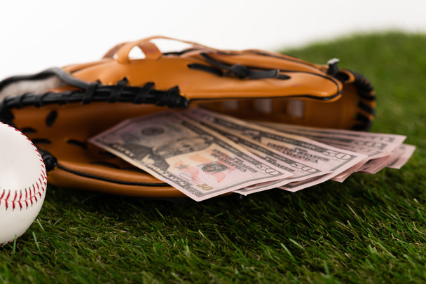 επιλεκτική εστίαση των τραπεζογραμματίων δολαρίου στο γάντι του μπέιζμπολ στο πράσινο γρασίδι που απομονώνεται στο λευκό, έννοια αθλητικών στοιχημάτων - Φωτογραφία, εικόνα