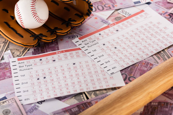 betting lists near baseball bat, glove and ball on euro and dollar banknotes, sports betting concept - Фото, зображення