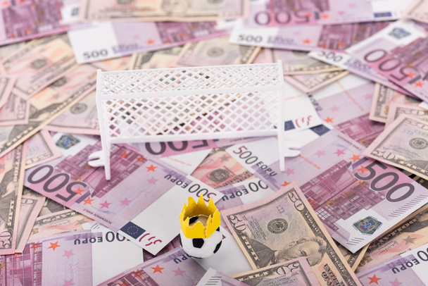 toy soccer ball with paper crown near miniature football gates on euro and dollar banknotes, sports betting concept - Φωτογραφία, εικόνα
